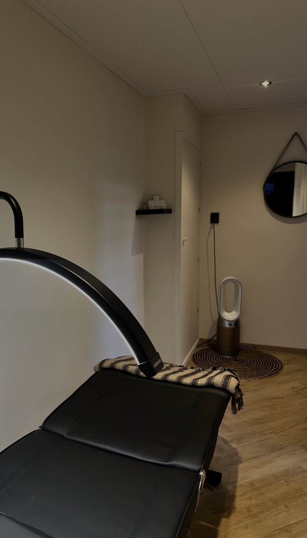 De behandelruimte: een zwarte behandelstoel onder een ronde lamp in een lichte kamer met een ronde spiegel